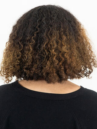 Foto del prima: donna vista da dietro con capelli neri corti e ricchi con radici visibili prima del colore.